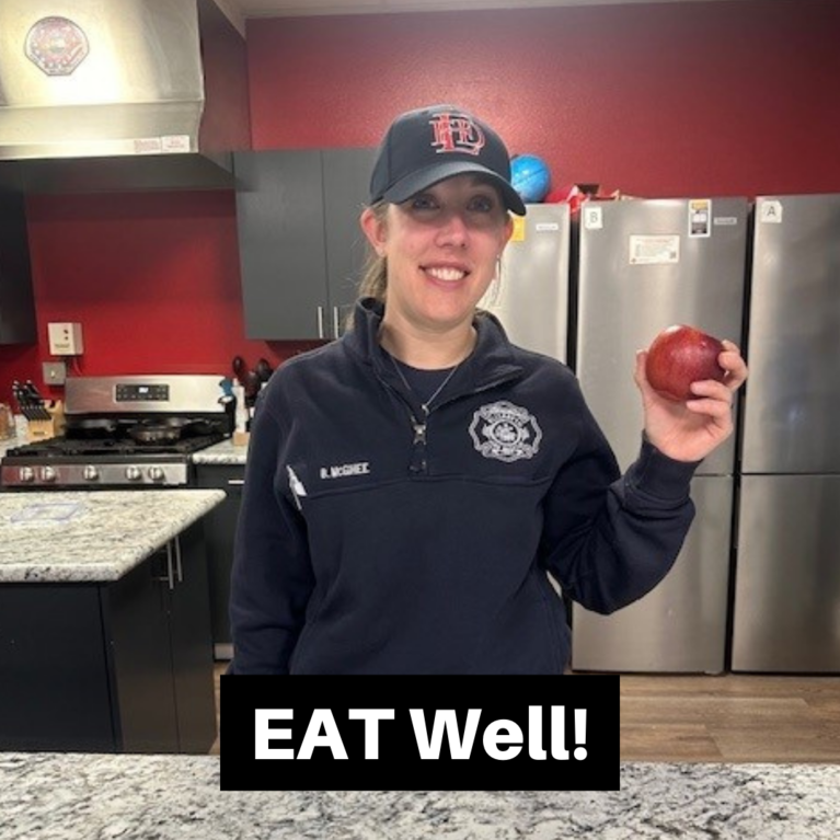 A firefighter holding an apple with the caption "EAT Well!"