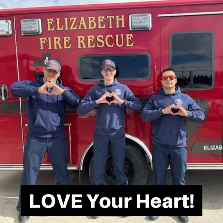 Firefighters standing in front of an ambulance making hearts with their hands with the caption "LOVE Your Heart!"