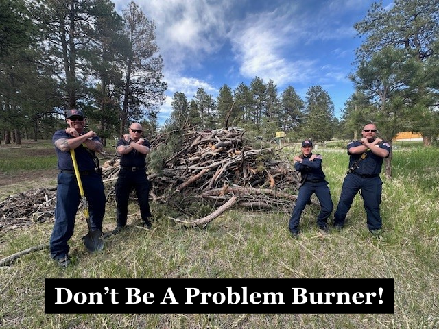 Firefighters standing in front of a large burn pile with their arms crossed with the caption "Don't Be A Problem Burner!"
