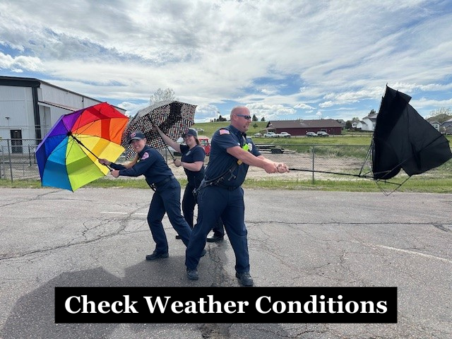Firefighters holding umbrellas that are being blown by the wind with the caption "Check Weather Conditions"