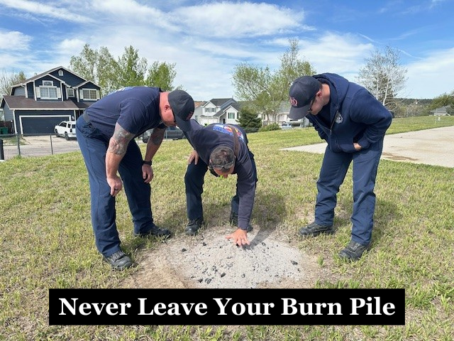 Firefighters checking a pile of ashes with the caption "Never Leave Your Burn Pile"
