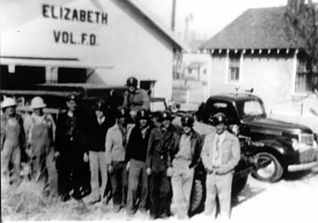 Black and white photo of firefighters standing in front of a volunteer fire station