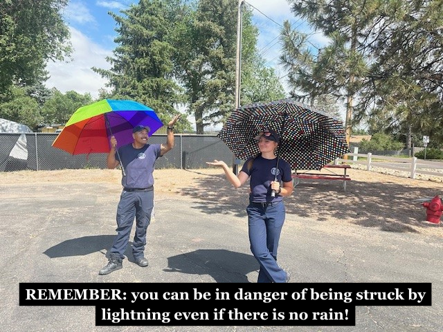 Firefighters standing outside and holding umbrellas with the caption "REMEMBER: you can be in danger of being struck by lightning even if there is no rain!"