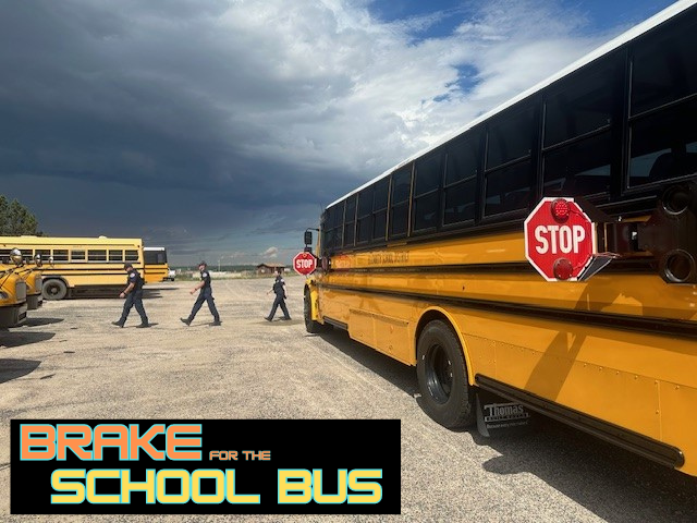 Firefighters crossing the street in front of a school bus with its stop sign extended with the caption "Brake for the School Bus"