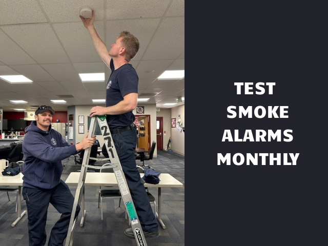 Firefighters testing a smoke alarm with the caption "Test Smoke Alarms Monthly"