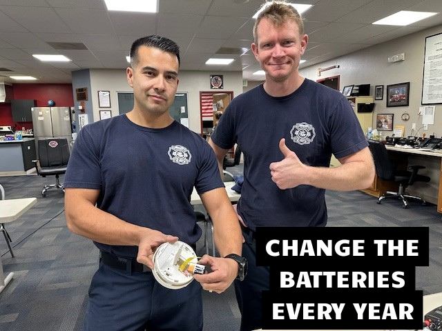 Firefighters changing smoke alarm batteries with the caption "Change The Batteries Every Year"