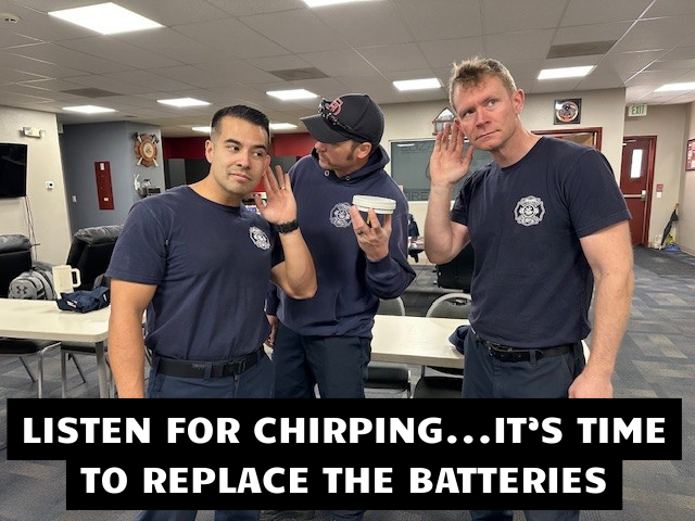 Firefighters listening to the sound coming from a smoke alarm with the caption "Listen For Chirping...It's Time To Replace The Batteries"