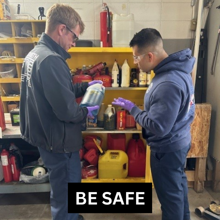 Two firefighters holding chemical cleaner with gloved hands and reading the label with the caption "Be Safe."