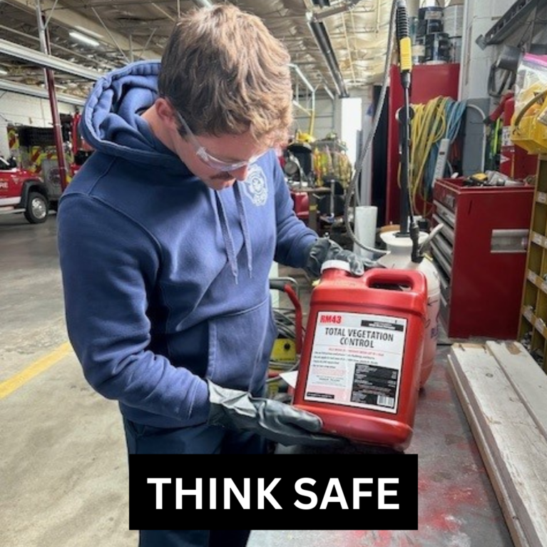 A firefighter holding a bottle of chemical cleaner with gloved hands and reading the label with the caption "Think Safe."
